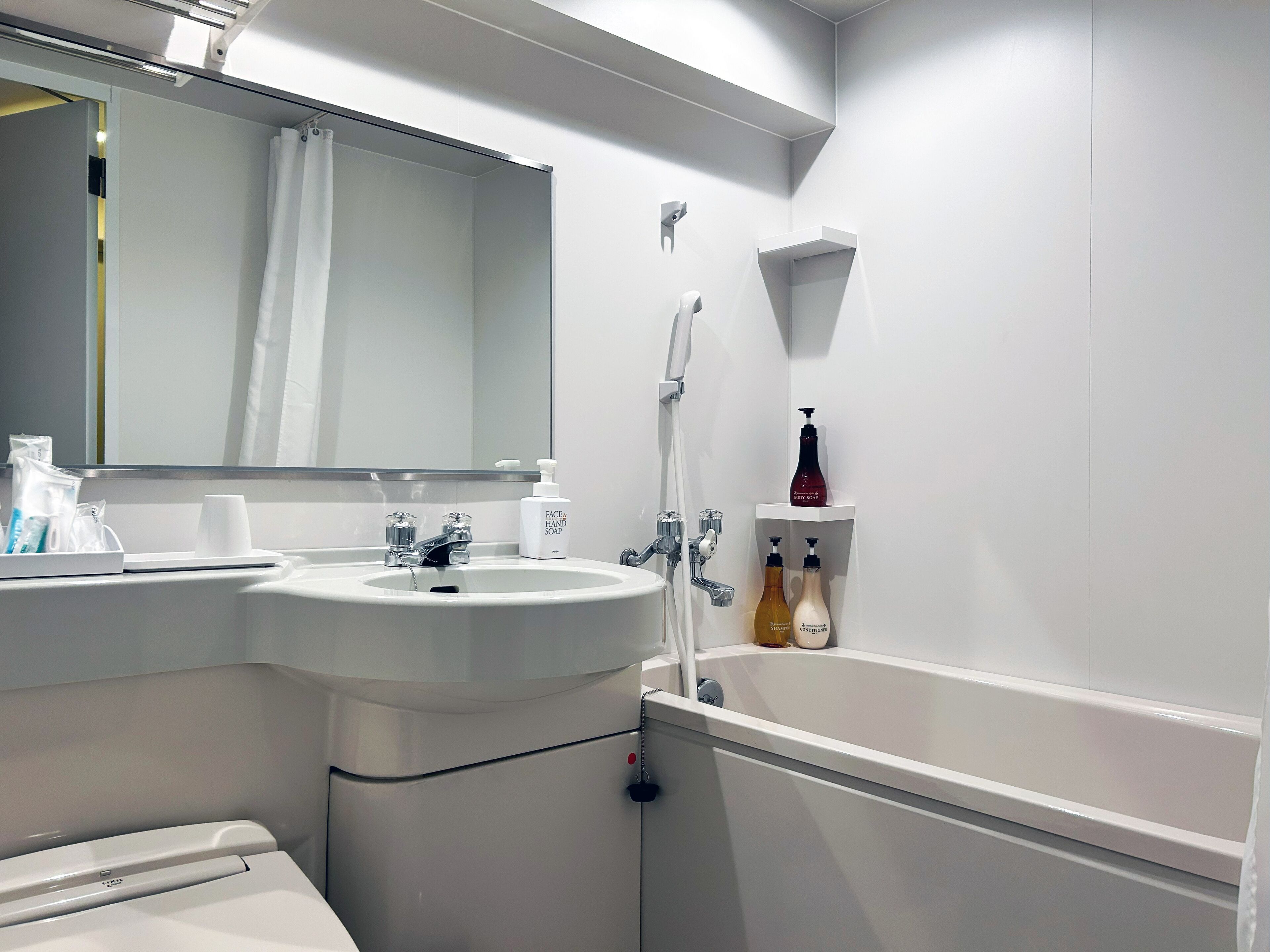 Une salle de bain moderne avec un lavabo blanc, un miroir, une douche et une étagère contenant des articles de toilette.