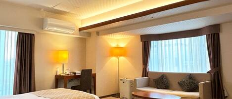 A hotel room with two beds, a desk with a lamp, a sofa, and a small table.