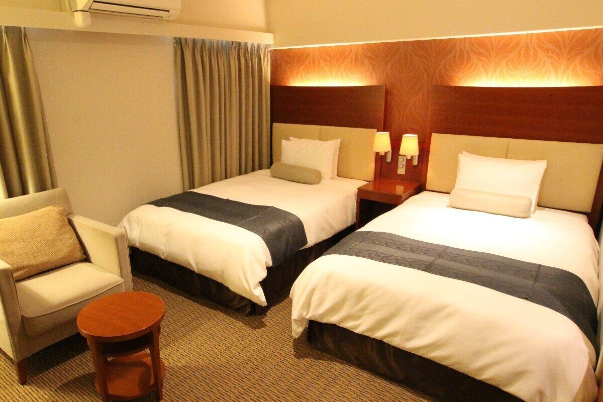 Ein Hotelzimmer mit zwei Betten, einer Couch, einem kleinen Tisch und einem Kopfteil mit integrierter Beleuchtung.