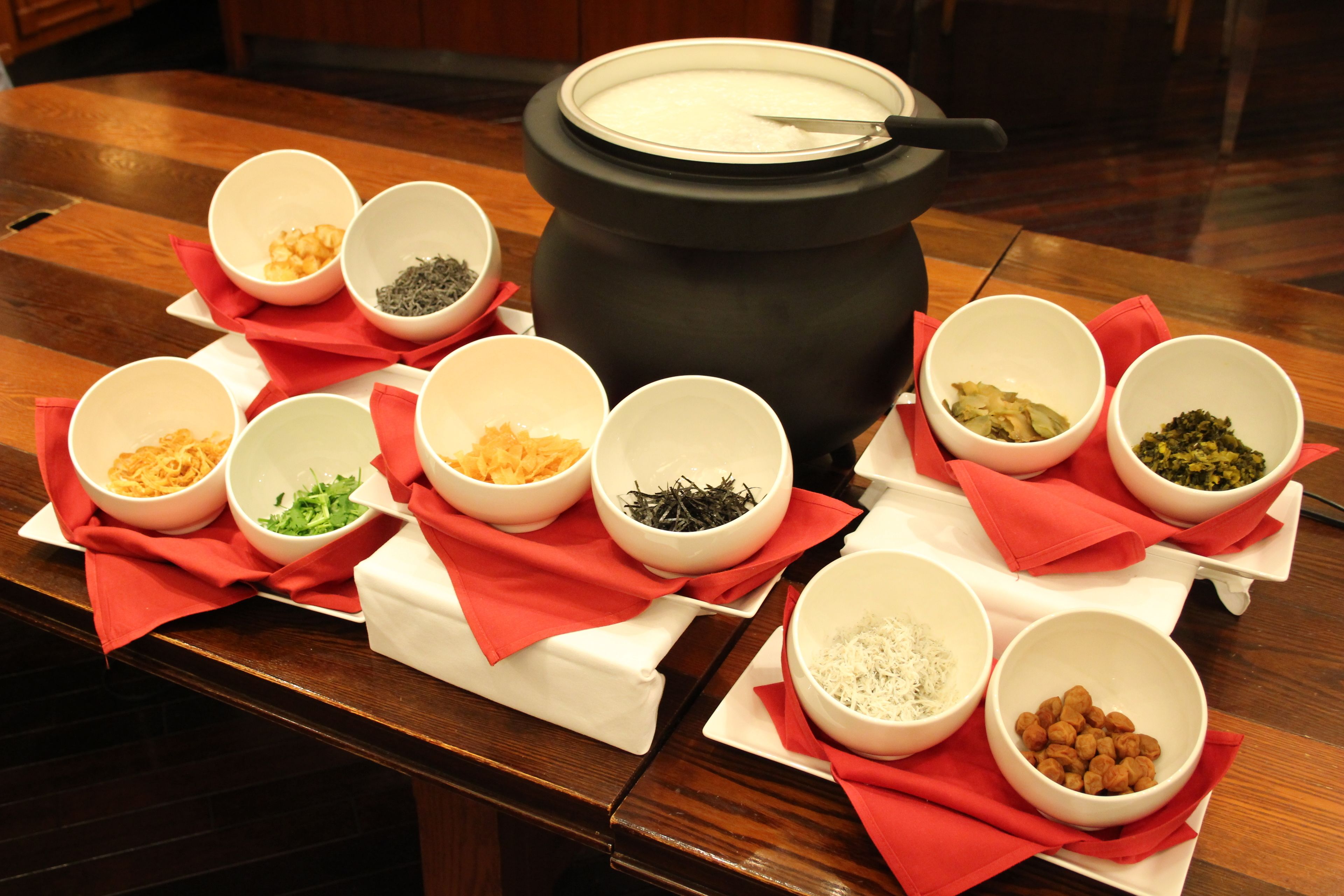 A table with various bowls of food ingredients and a large pot on a wooden table.