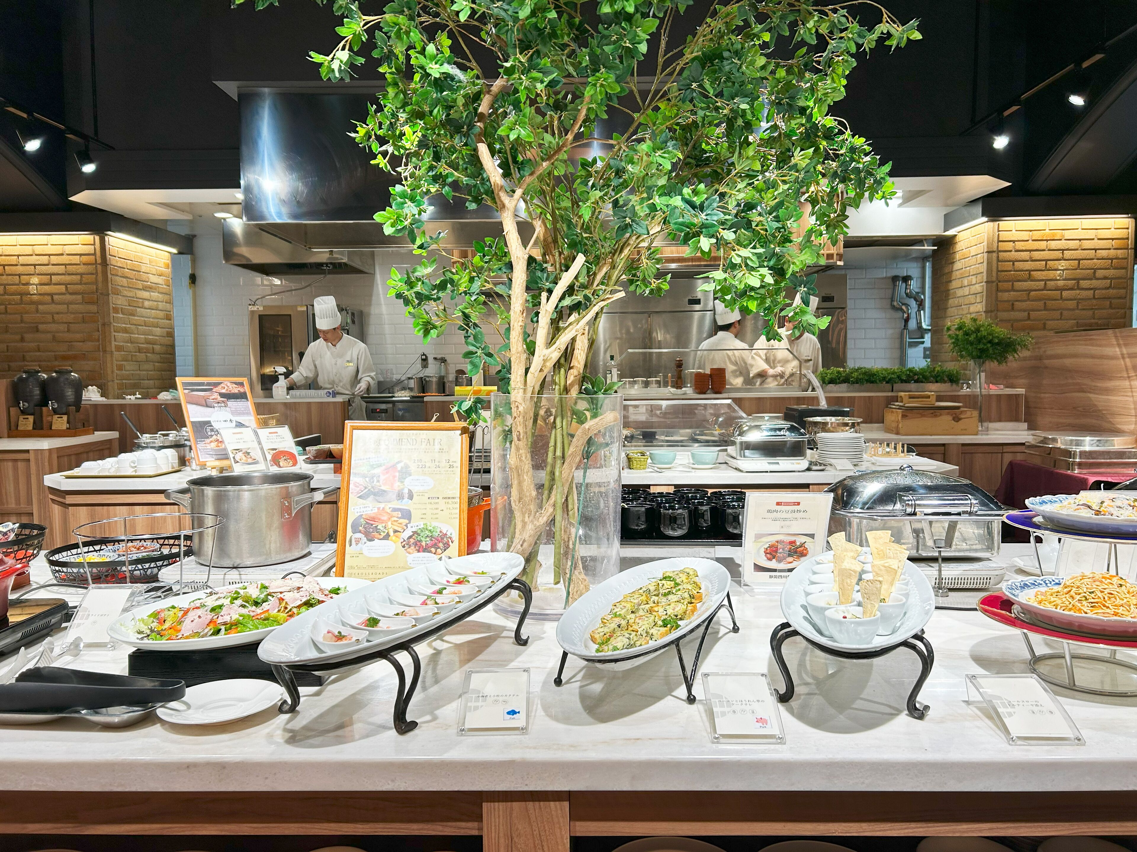 A buffet setup with various dishes, a menu board, and a chef preparing food in the background.
