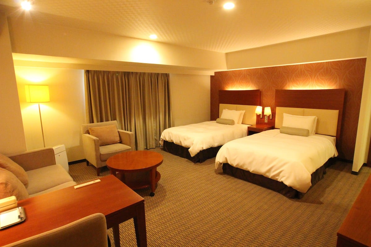 A hotel room with two beds, a sofa, a small table, and a lamp.