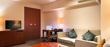 A hotel room with a TV, a sofa, a small table, and a red coffee table.