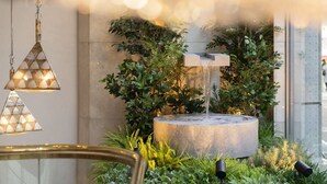 A modern indoor garden with a water feature, hanging lights, and lush greenery. - Nakajimaya Grand Hotel (Shizuoka)
