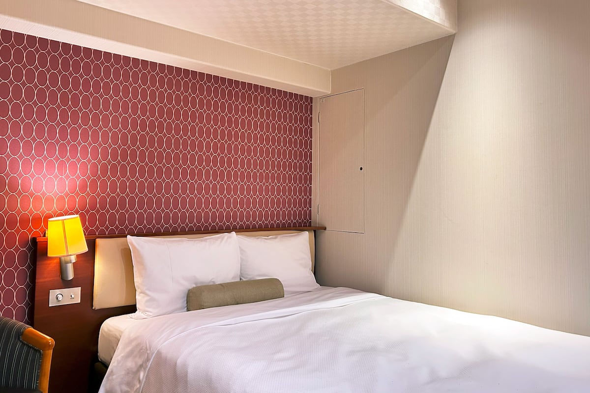 A hotel room with a bed, a nightstand with a lamp, and a patterned wall.