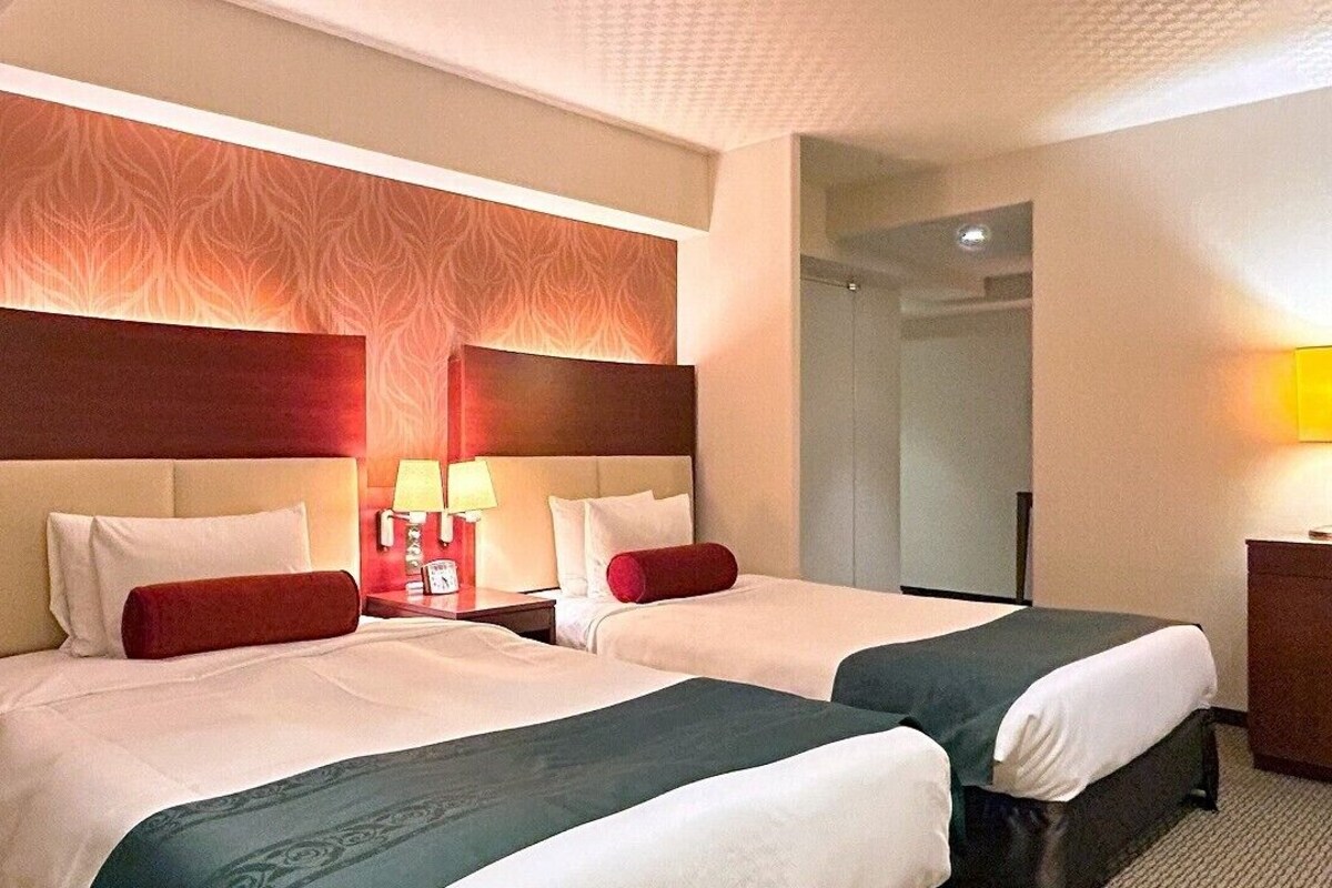 Ein Hotelzimmer mit zwei Betten, einem Nachttisch mit Lampen und einem Spiegel.