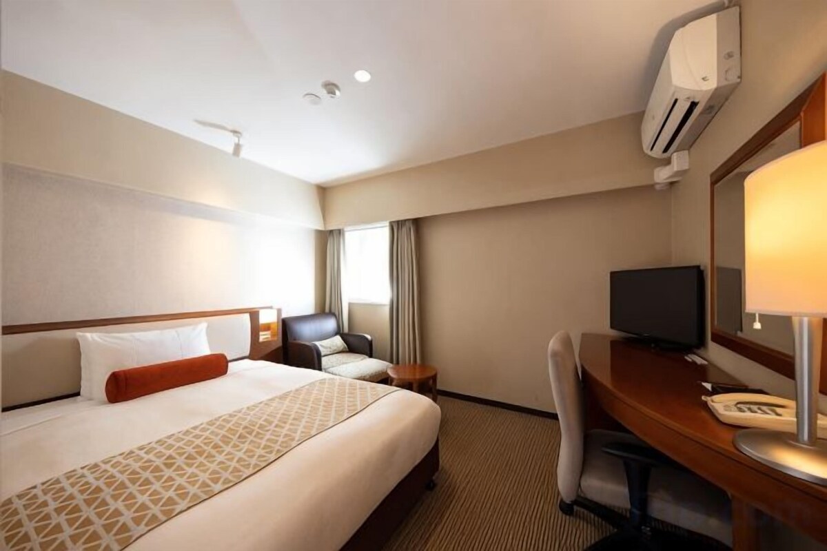 Ein Hotelzimmer mit Bett, Schreibtisch, Stuhl, Fernseher und Spiegel.