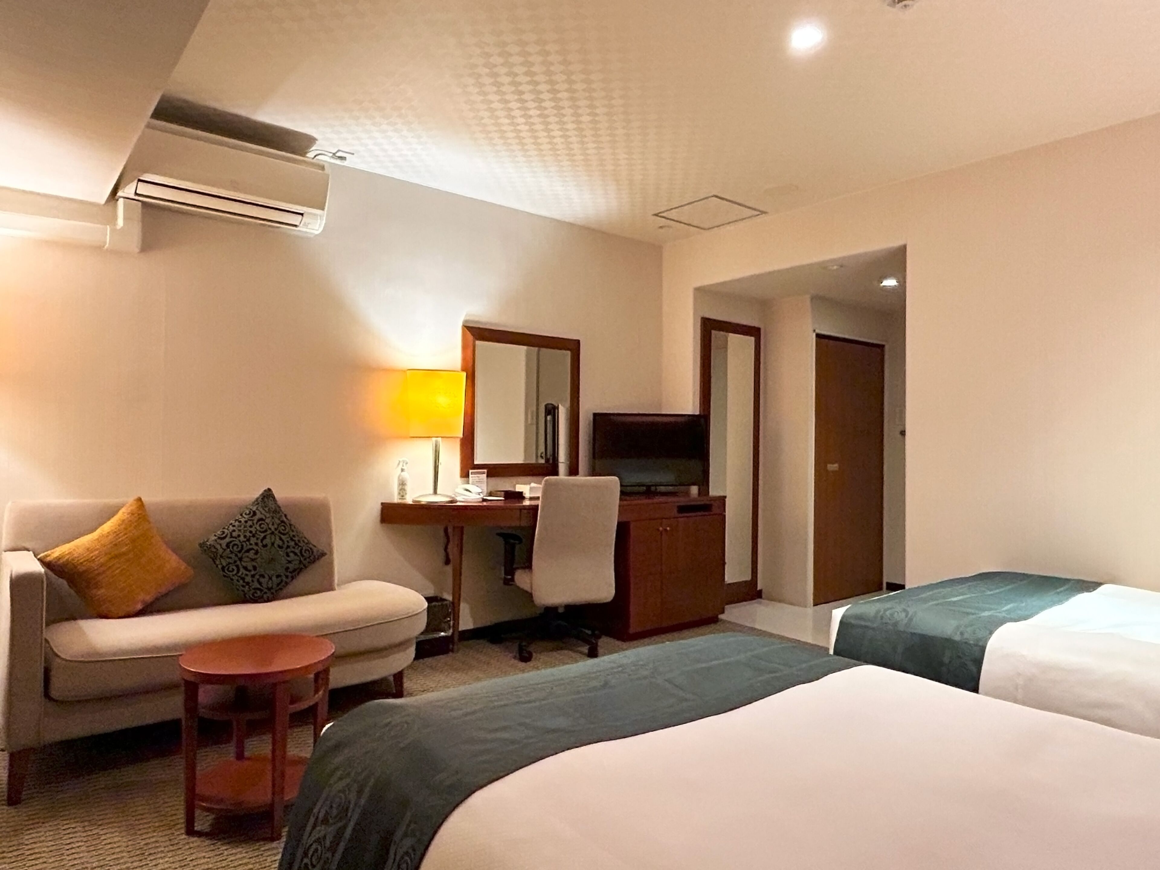 A hotel room with a sofa, a desk, a television, and two beds.