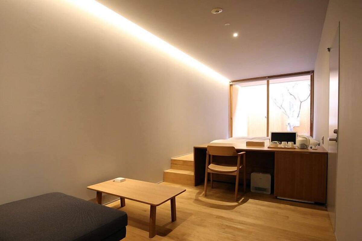 Quarto compacto com escrivaninha, cadeira e mesa pequena.
