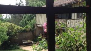 A view through a window of a rustic building with a garden in the foreground and a wooden fence. - Jouandassou (Fontrailles)