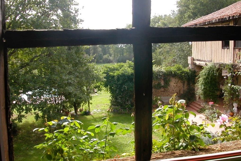 Vista a través de una ventana que muestra un jardín con una casa de madera al fondo.