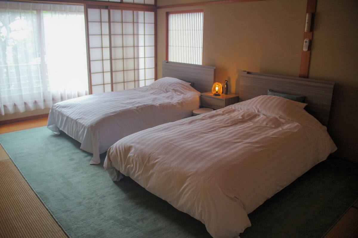 A room with two beds, a nightstand with a lamp, and a sliding shoji screen.