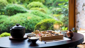 A table with a teapot, bowls, and a wooden box, set against a window with a view of a lush garden. - Barcos Ryokan Misasaso (Misasa)