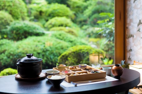 A table with a teapot, bowls, and a wooden box, set against a window with a view of a lush garden.