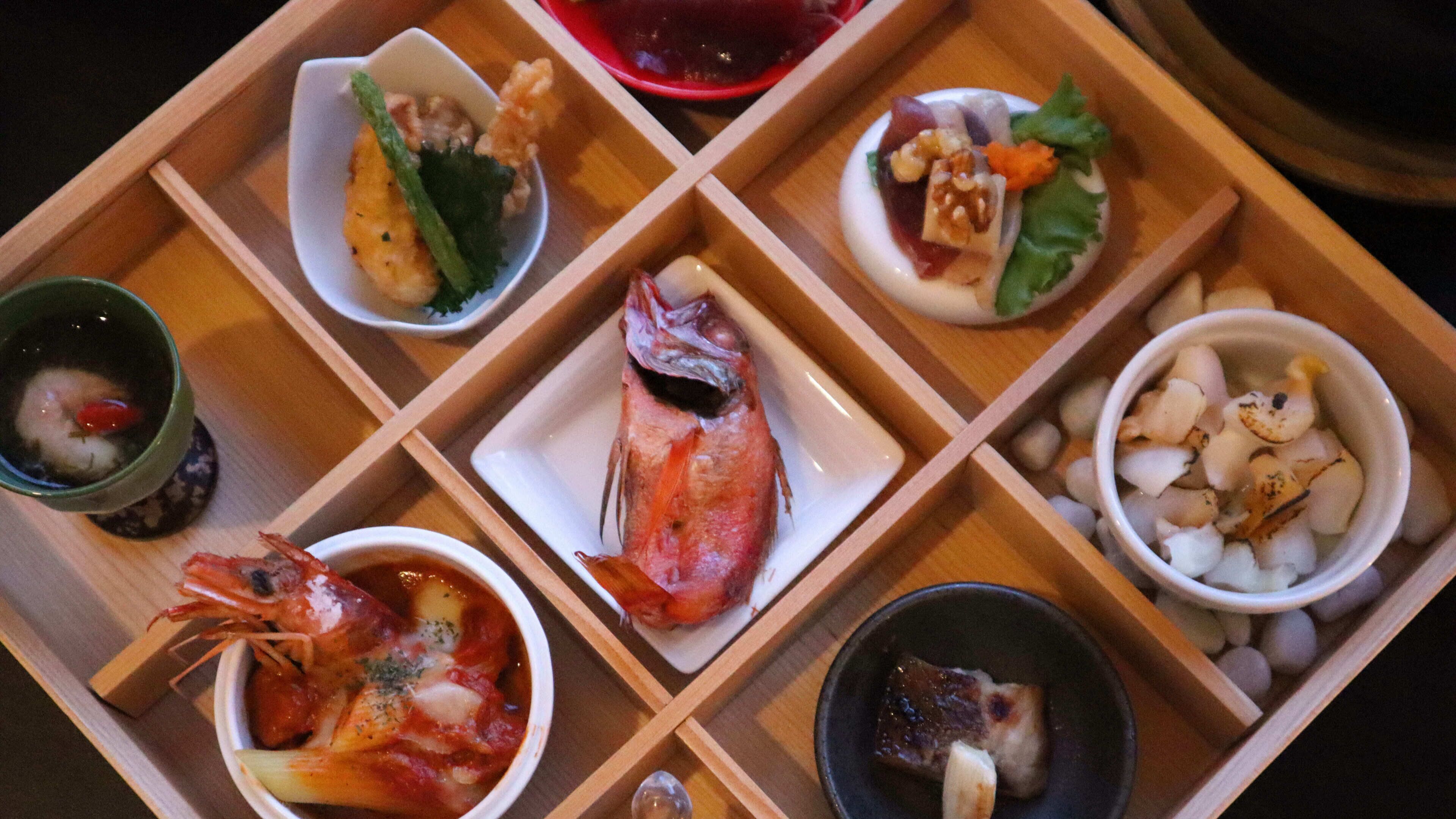 A wooden tray with various dishes including seafood, vegetables, and a bowl of soup.