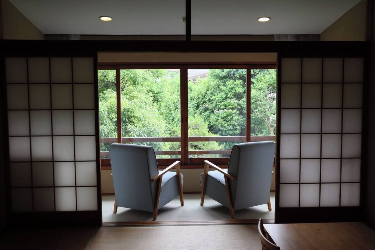 A room with two chairs facing a large window with a view of greenery.