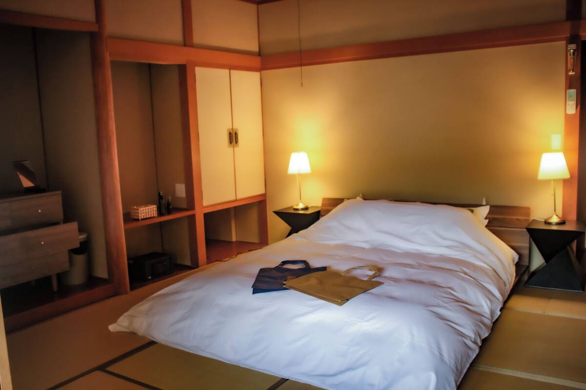 A hotel room with a bed, two bedside lamps, a wardrobe, and a small table.
