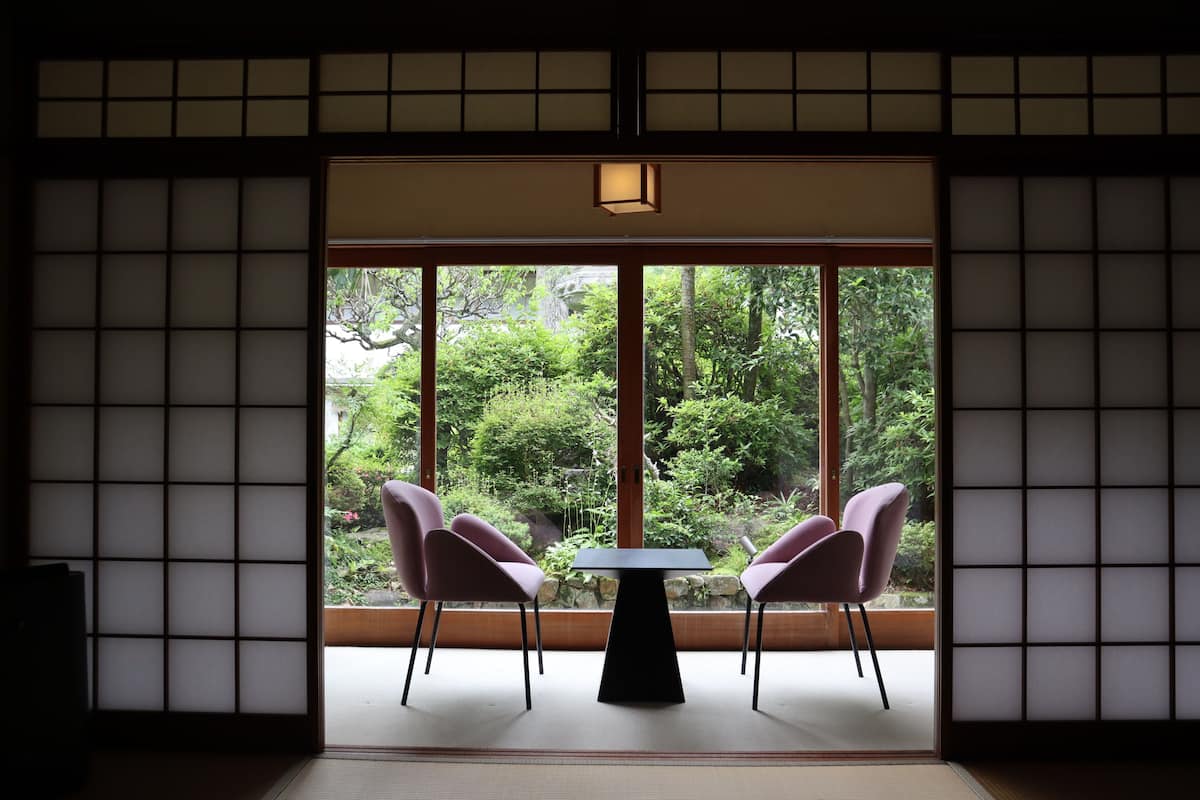 A traditional Japanese room with tatami flooring, a low table, and two chairs.