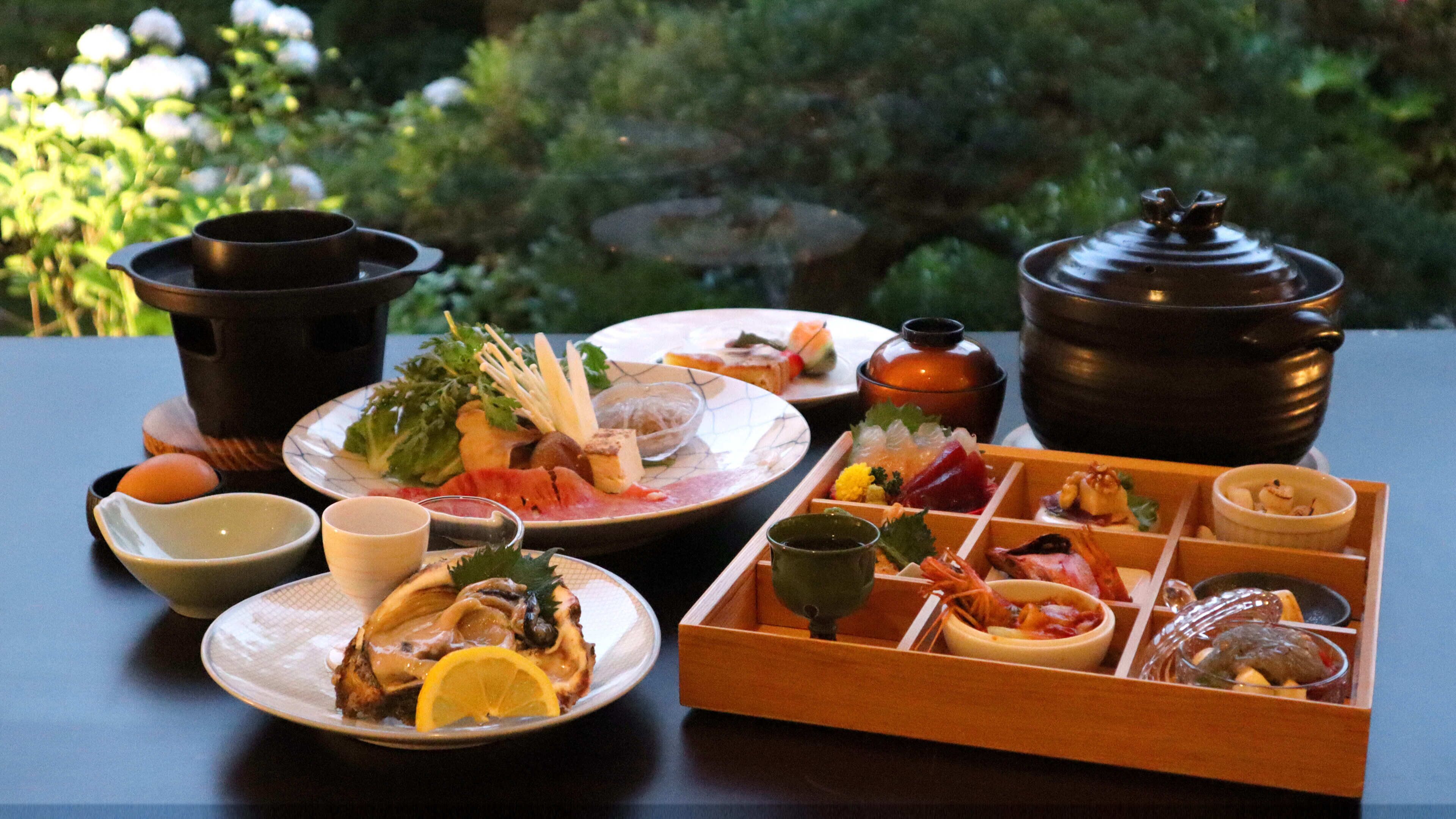 Ein Tisch mit verschiedenen Speisen und einem Teekessel, draußen arrangiert mit Grünpflanzen im Hintergrund.