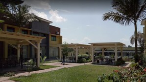 A courtyard with outdoor seating, palm trees, and a building with a sign reading "ETH CLUB". - Courtyard International Hotel (Lyantonde)