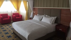 A hotel room with a large bed, two red armchairs, a wooden headboard, and a patterned carpet. - Courtyard International Hotel (Lyantonde)