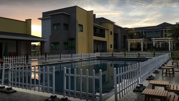 A modern building with a swimming pool surrounded by a white fence, outdoor seating, and a covered area. - Courtyard International Hotel (Lyantonde)