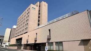A multi-story building with a modern architectural design, featuring a prominent entrance with a glass facade and a parking area in front. - Sunroute Tokuyama (Shunan)