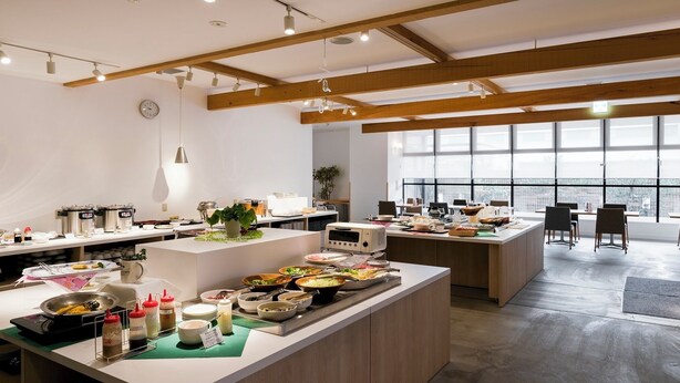 A modern kitchen with a central island, multiple cooking stations, and large windows providing natural light.