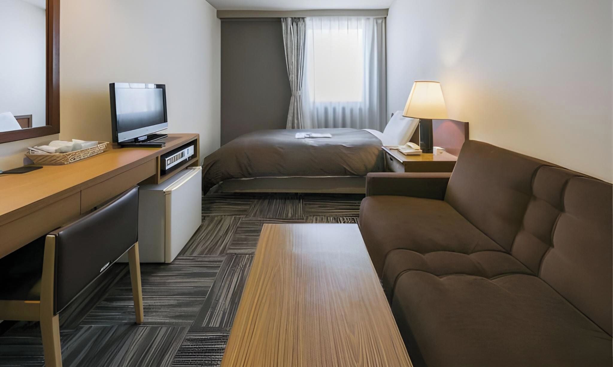 Une chambre d’hôtel comprenant un lit, un canapé, un bureau avec une télévision, une lampe et un petit réfrigérateur.