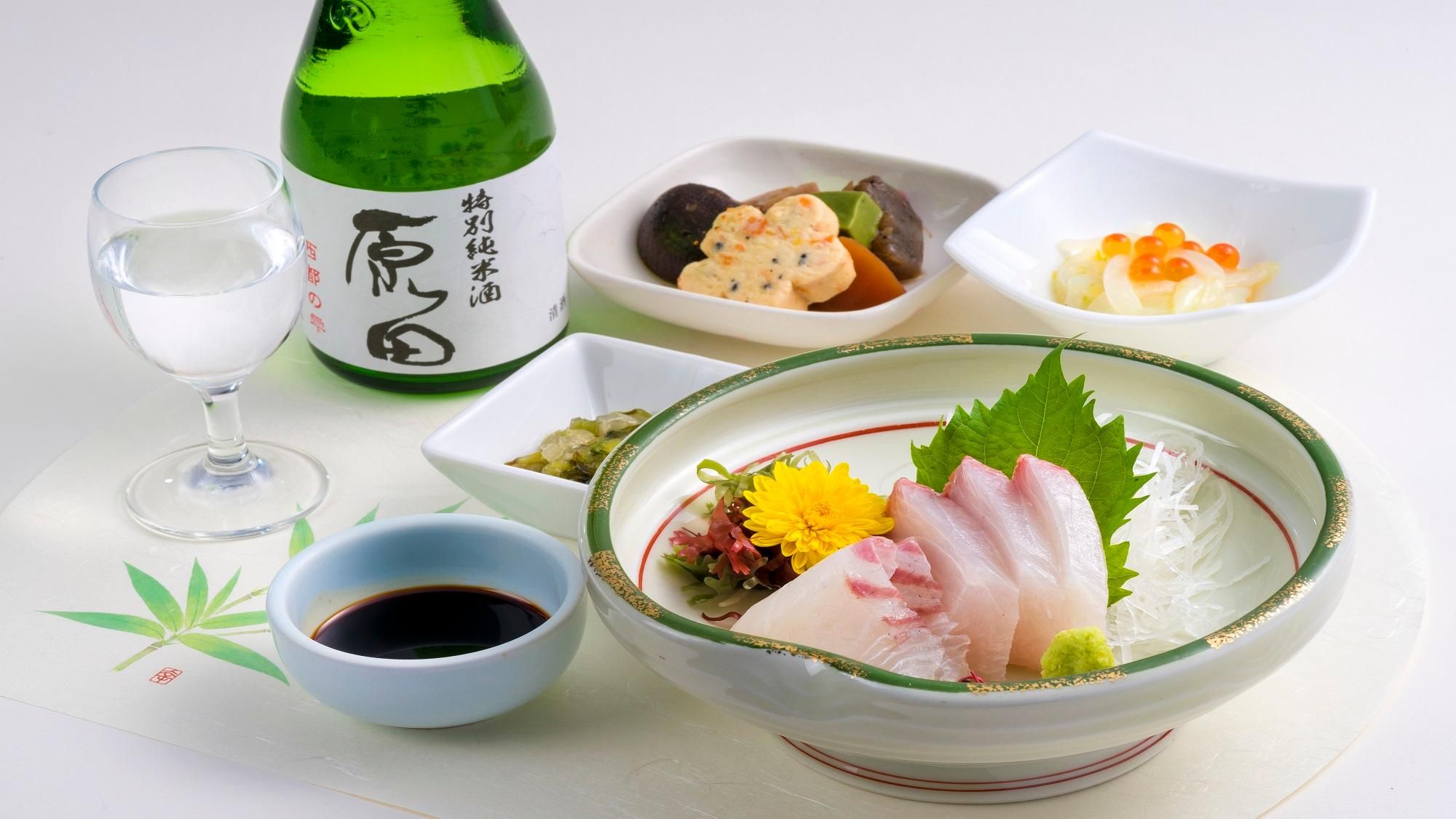 A traditional Japanese meal with a bottle of sake, a glass of water, and various dishes including sashimi and pickled vegetables.