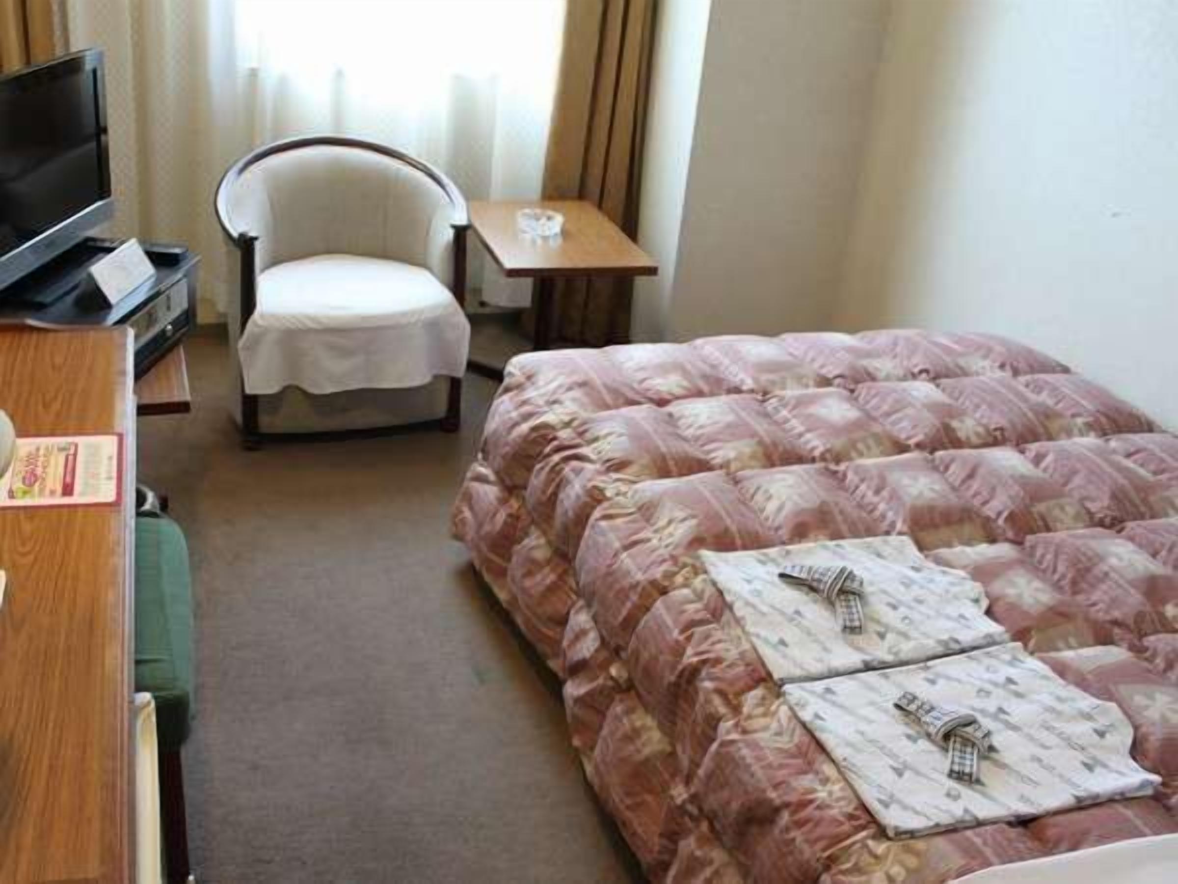A hotel room with a bed, a chair, a small table, and a TV.