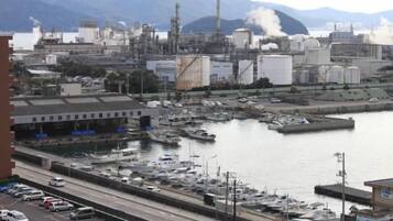 A marina with boats docked, a road with vehicles, and industrial buildings in the background.