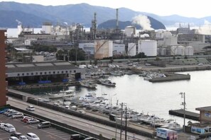 A marina with boats docked, a road with vehicles, and industrial buildings in the background. - Sunroute Tokuyama (Shunan)