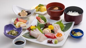 A variety of sushi and sashimi on a white plate with small bowls of soy sauce, pickled ginger, and wasabi. - Sunroute Tokuyama (Shunan)