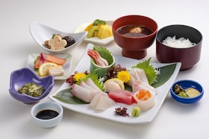 A variety of sushi and sashimi on a white plate with small bowls of soy sauce, pickled ginger, and wasabi. - Sunroute Tokuyama (Shunan)