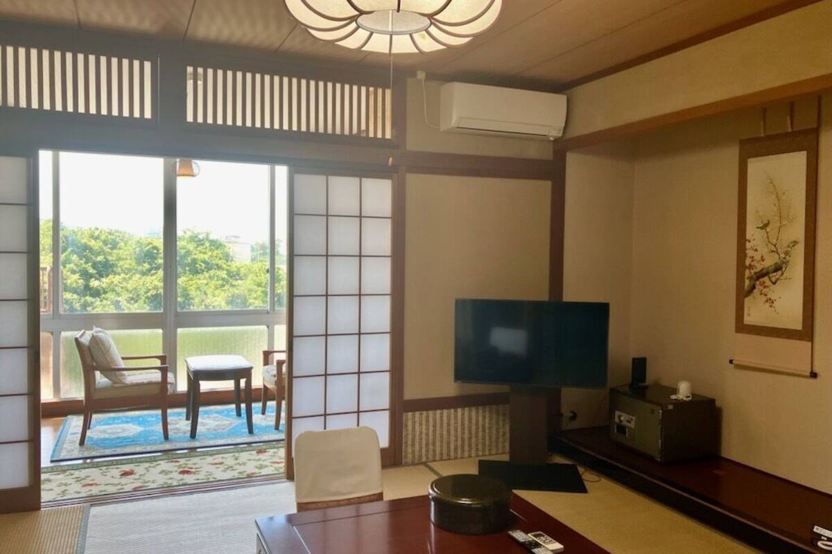Una habitación tradicional japonesa con suelo de tatami, televisión, sofá y puerta corrediza que da a un balcón.