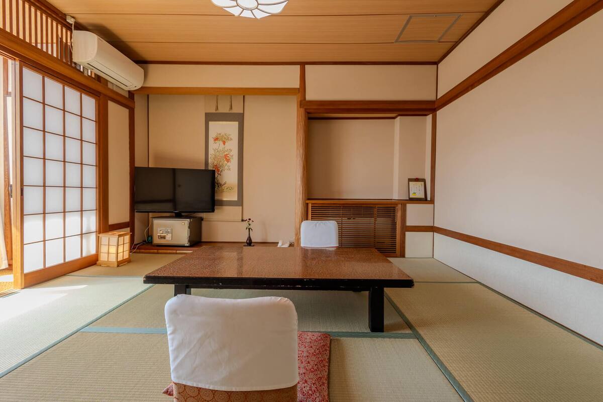 Una habitación tradicional japonesa con suelo de tatami, una mesa baja, un televisor y una puerta corredera.
