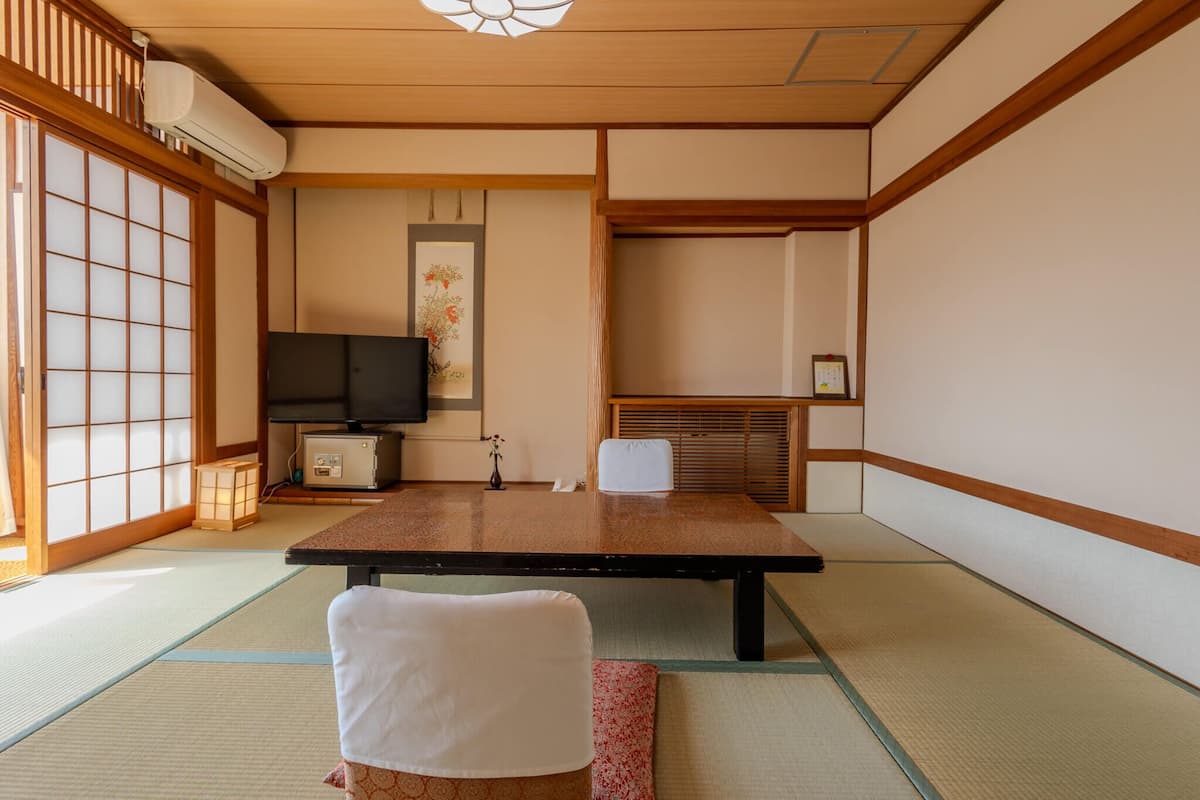 A traditional Japanese room with tatami flooring, a low table, a television, and a sliding door.