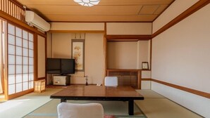 Een traditionele Japanse kamer met tatami vloerbedekking, een lage tafel, een televisie en een schuifdeur.