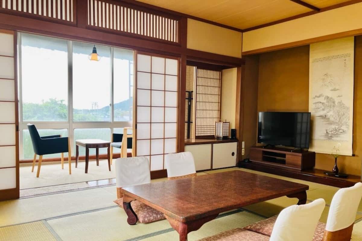 Una habitación japonesa tradicional con suelo de tatami, una mesa baja, sillas, un televisor y puertas correderas.