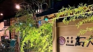 Een restaurant met een bord, terrasplek en bamboeplanten.