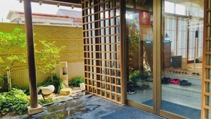 Een traditioneel Japans gebouw met een houten latticewerking entree, een betegeld terras en uitzicht op de straat.