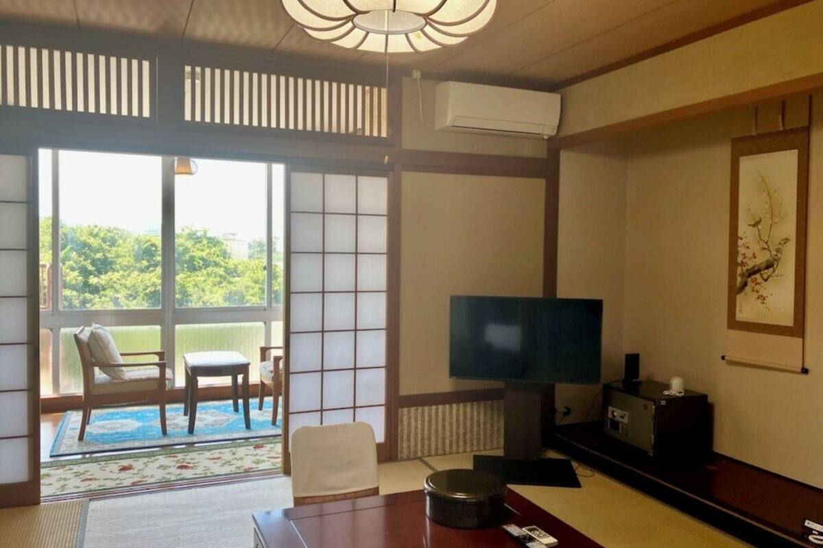 Una habitación tradicional japonesa con suelo de tatami, televisión, sofá y vistas al exterior.