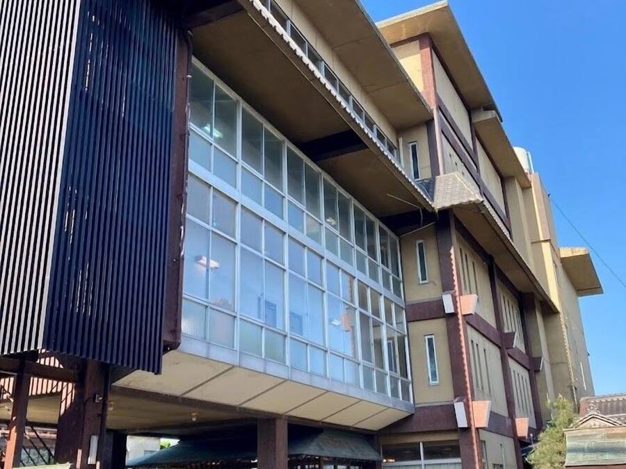 A multi-story building with large windows, a covered entrance, and a parking area with motorcycles.