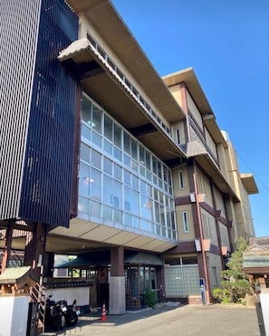 A multi-story building with large windows, a covered entrance, and a parking area with motorcycles.
