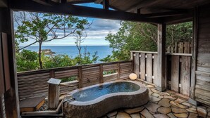 A wooden deck with a stone hot tub, a wooden bench, and a view of the ocean. - Hamadachidori no Yu Kaishu (Shirahama)