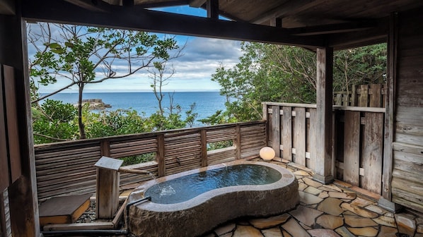 A wooden deck with a stone hot tub, a wooden bench, and a view of the ocean.