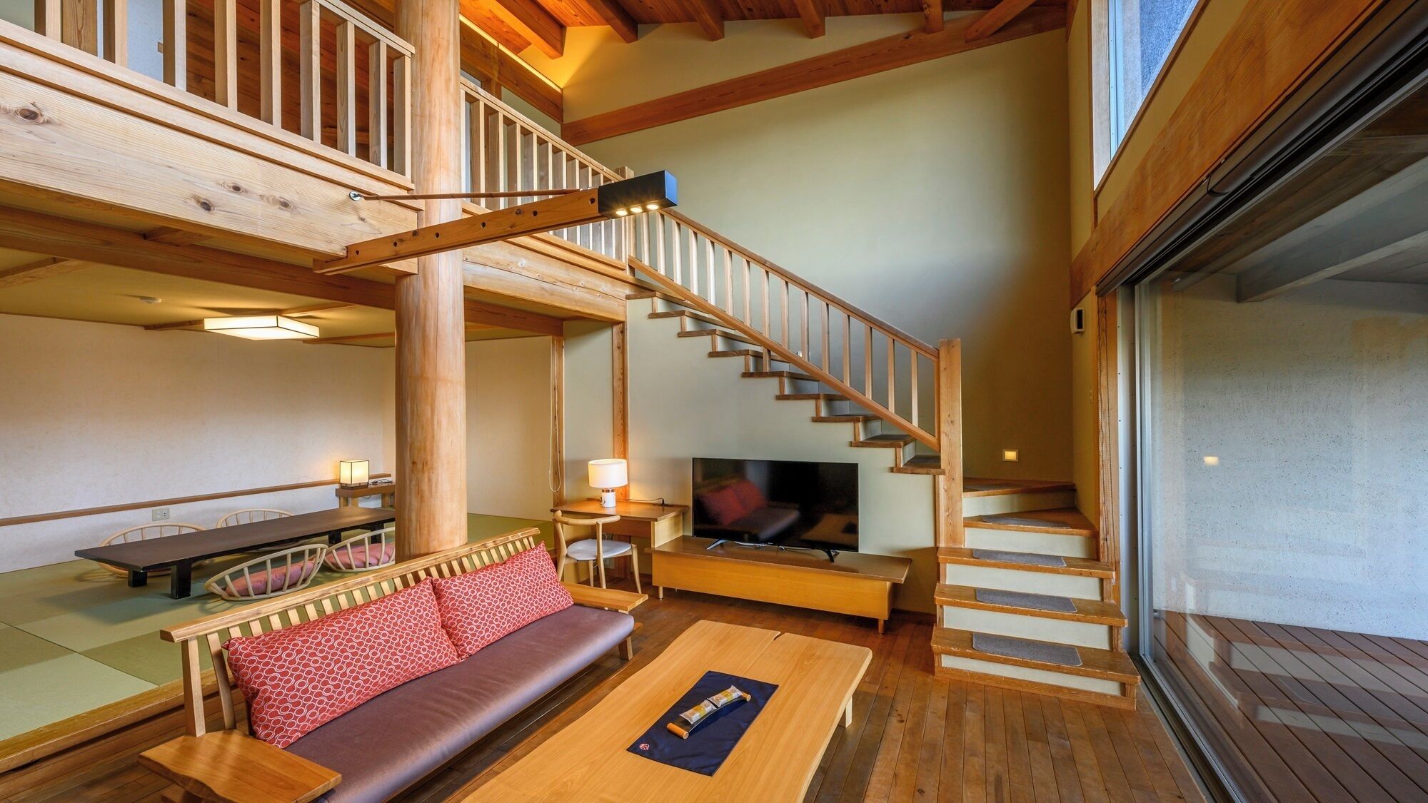 Ein Holzinnenraum mit Treppe, einer Couch, einem Fernseher und Tatami-Matten.