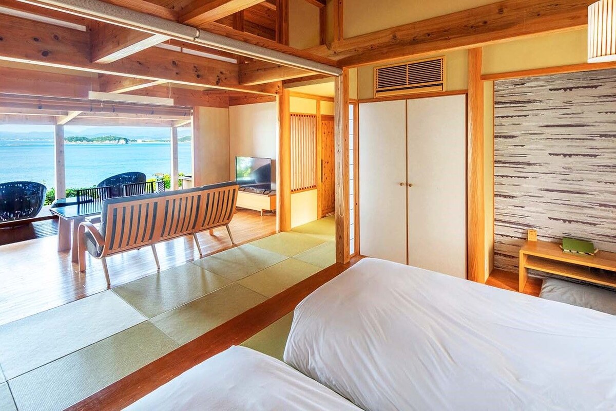 Ein Zimmer mit einem Bett, einem Fernseher, einer hölzernen Bank und Meerblick.
