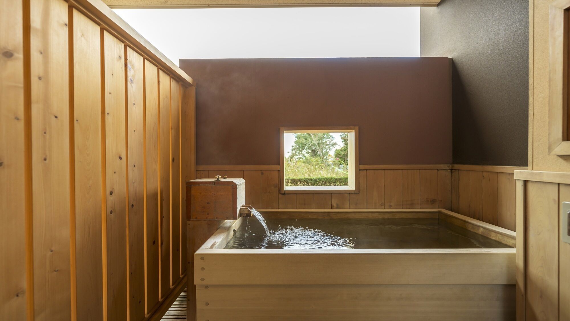 Eine Holzsauna mit Fenster, einer Holzbank und einem Wasserhahn.